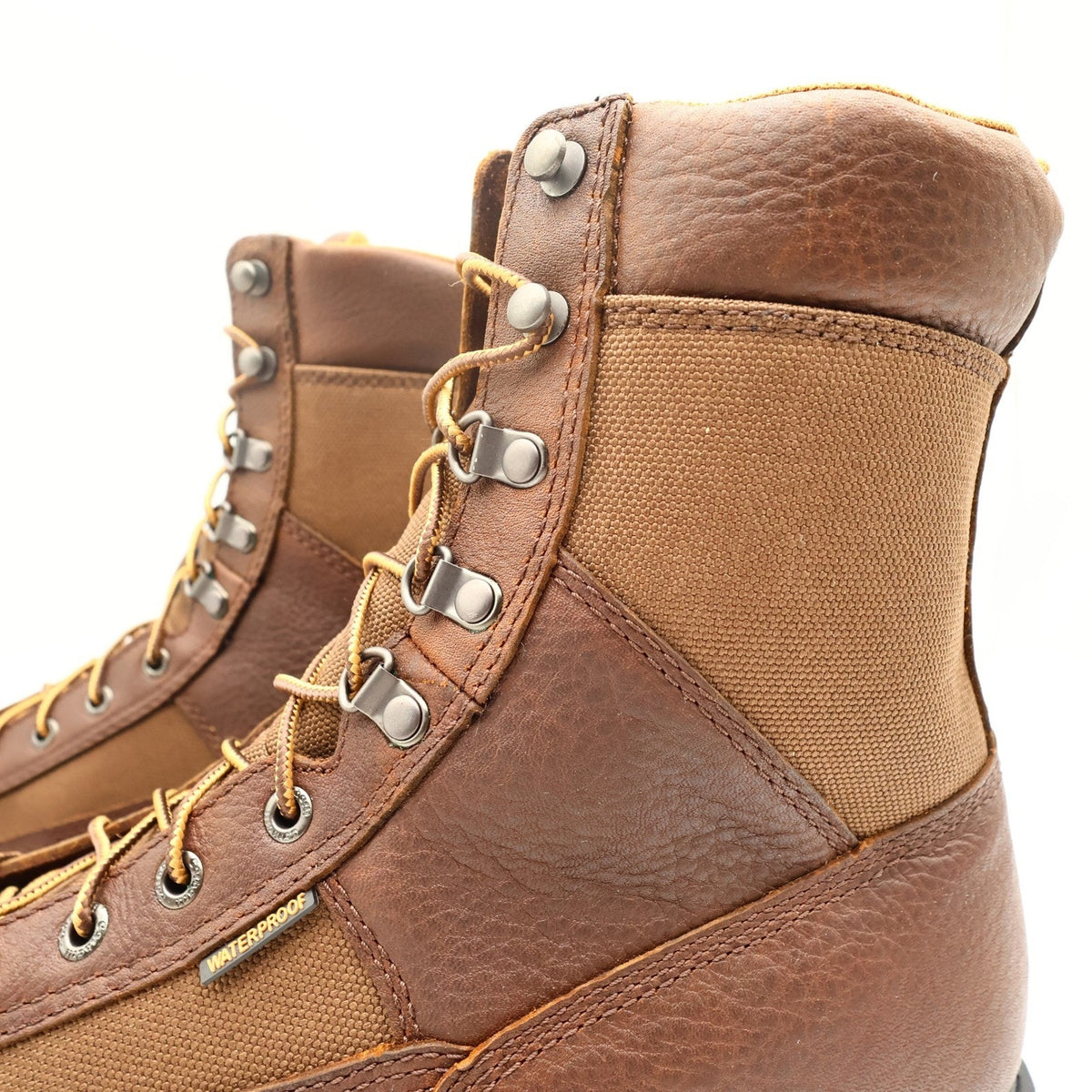 Close-up of pebbled brown leather, canvas panel, and metal speed hooks on Carhartt boot