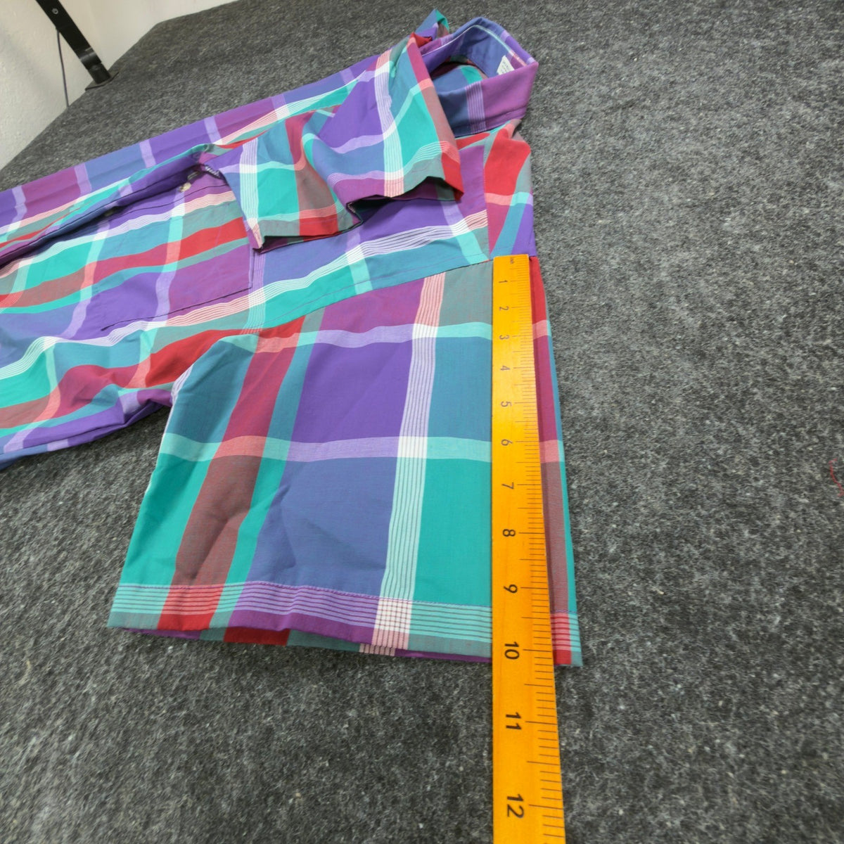 Purple, turquoise and red plaid 417 by Van Heusen shirt, short sleeve shown beside a ruler