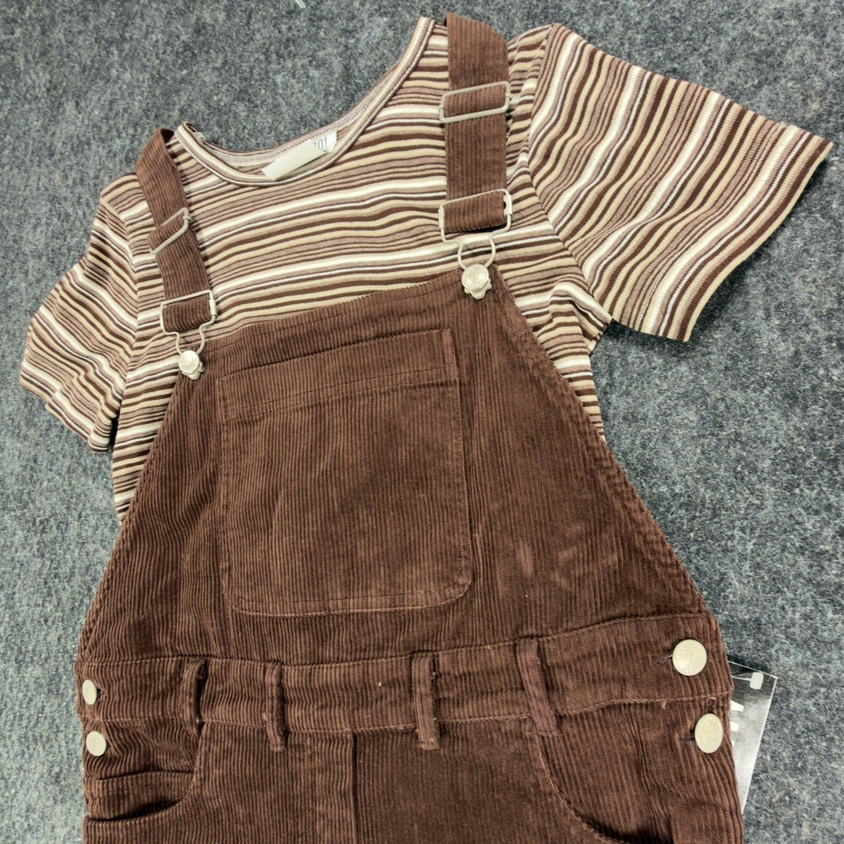 Angled close-up of the front bib, strap fasteners and striped top in a brown Amy Too jumper dress set
