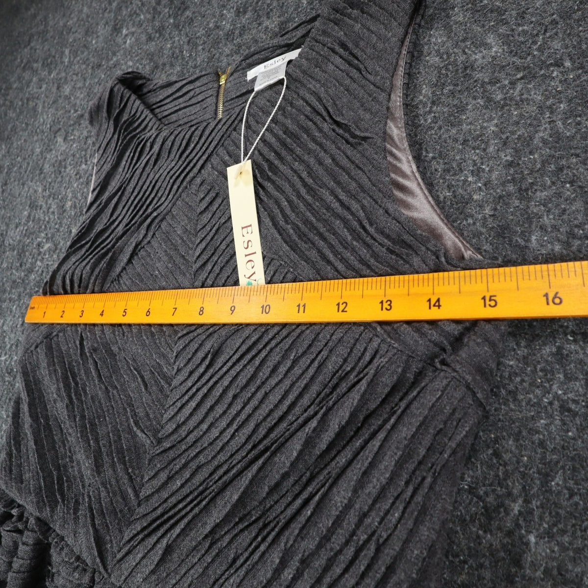 Ruler across the chest of charcoal gray Esley sleeveless dress with textured pleats and a black belt