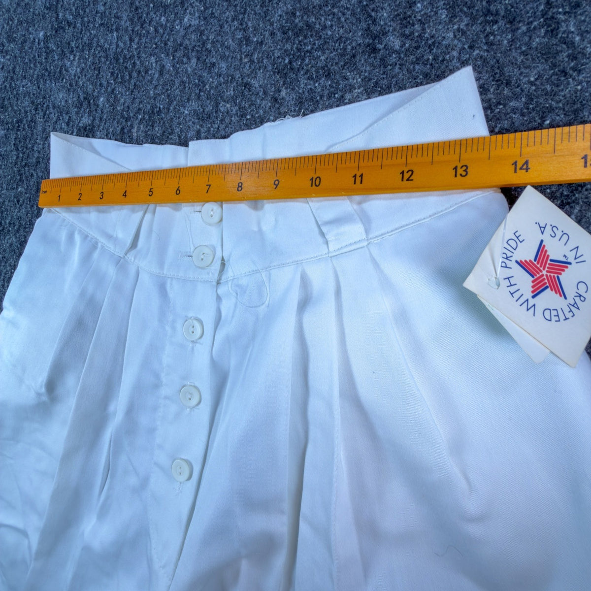 Ruler across the waistband of white Gazelle pleated shorts with a button front