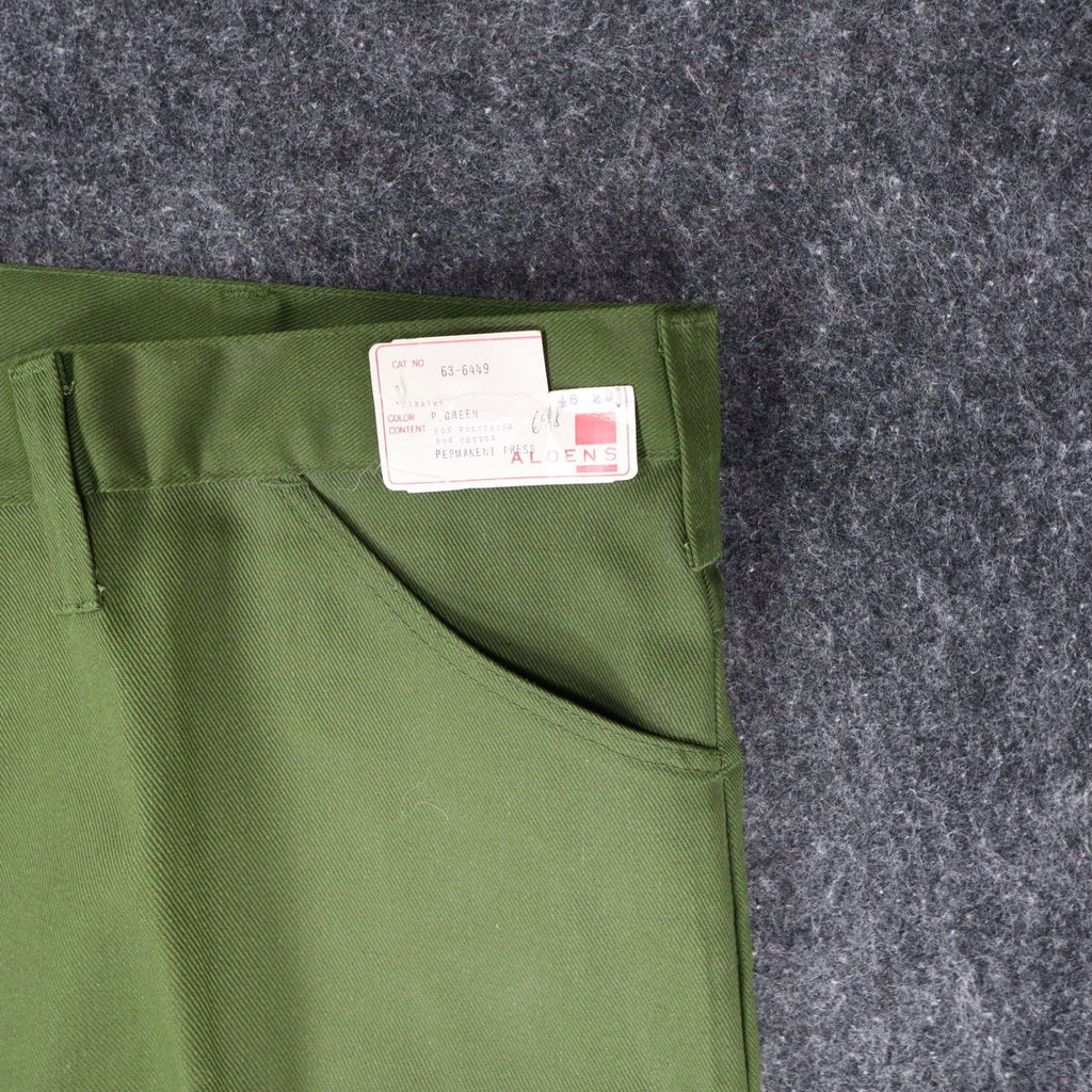 Close-up of a slanted front pocket and attached product label on green Aldens pants