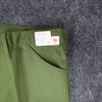 Close-up of a slanted front pocket and attached product label on green Aldens pants