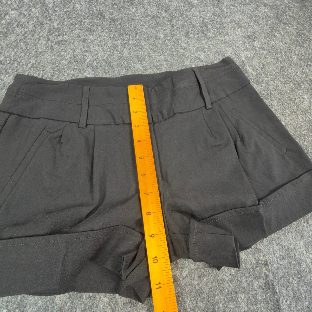 Ruler from the waistband to the crotch of black My Michelle pleated shorts with cuffed hems