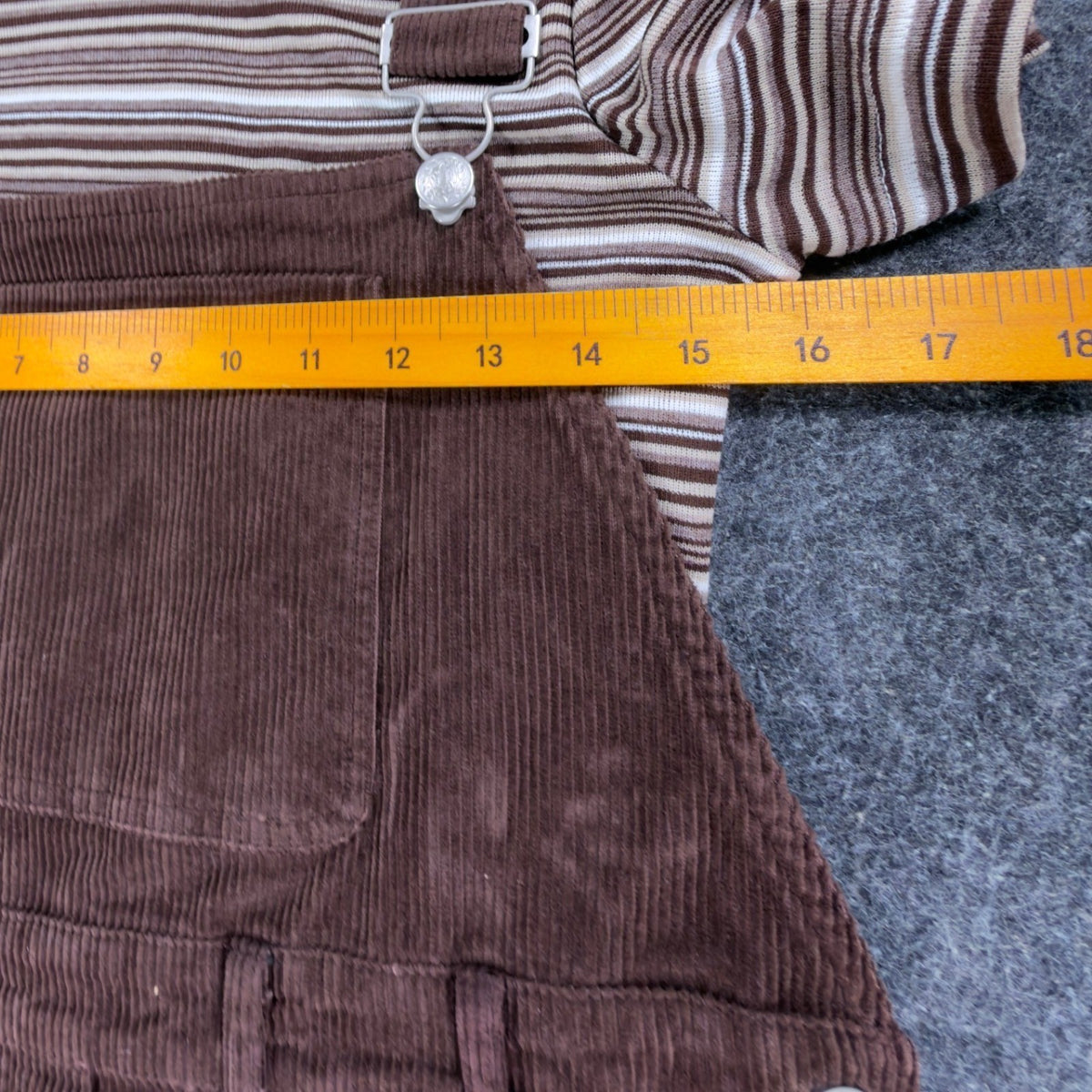 Ruler across the chest of a brown Amy Too jumper dress set, over the bib and striped top