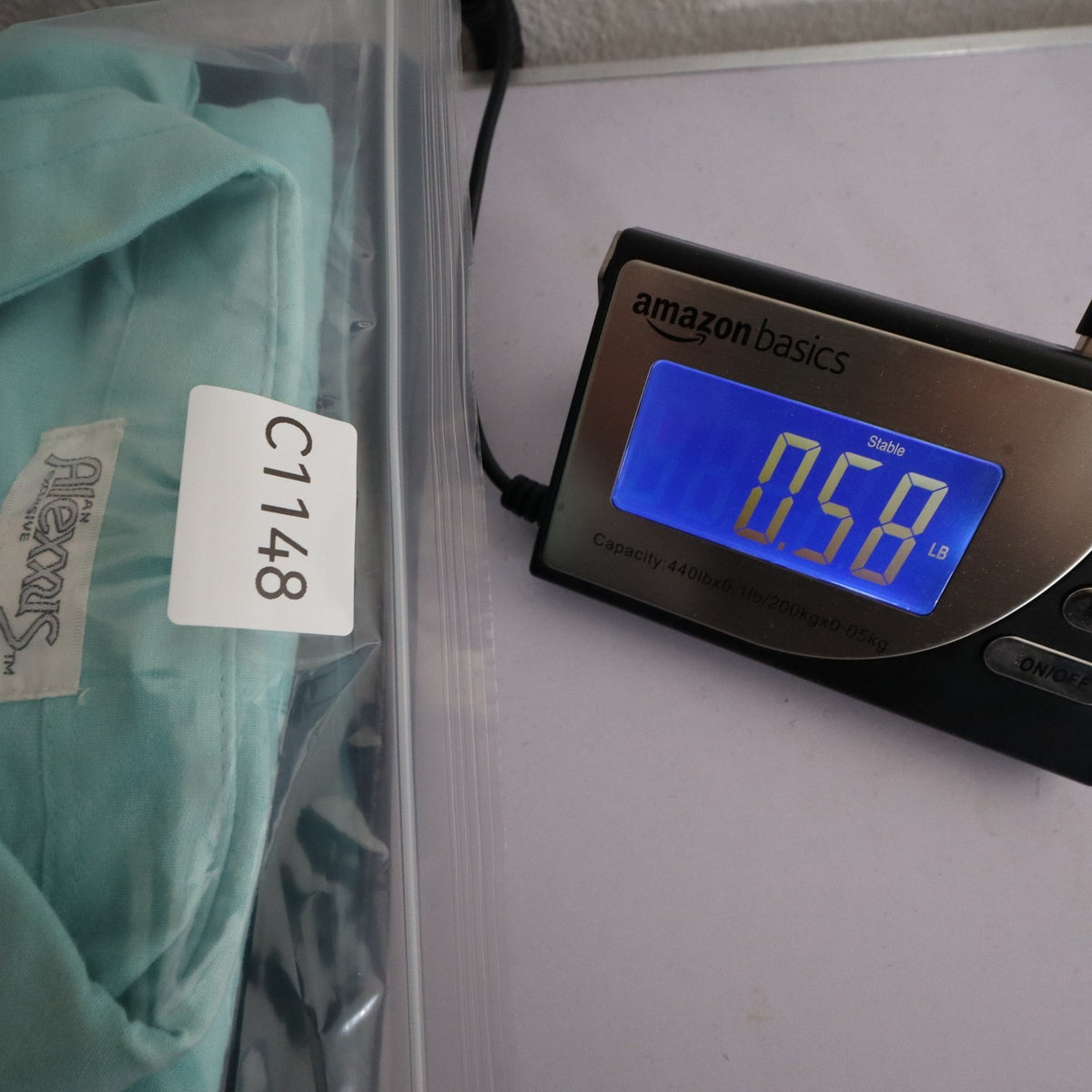 Aqua blue Alexxus short-sleeve shirt in an inventory-labeled clear bag beside a digital scale
