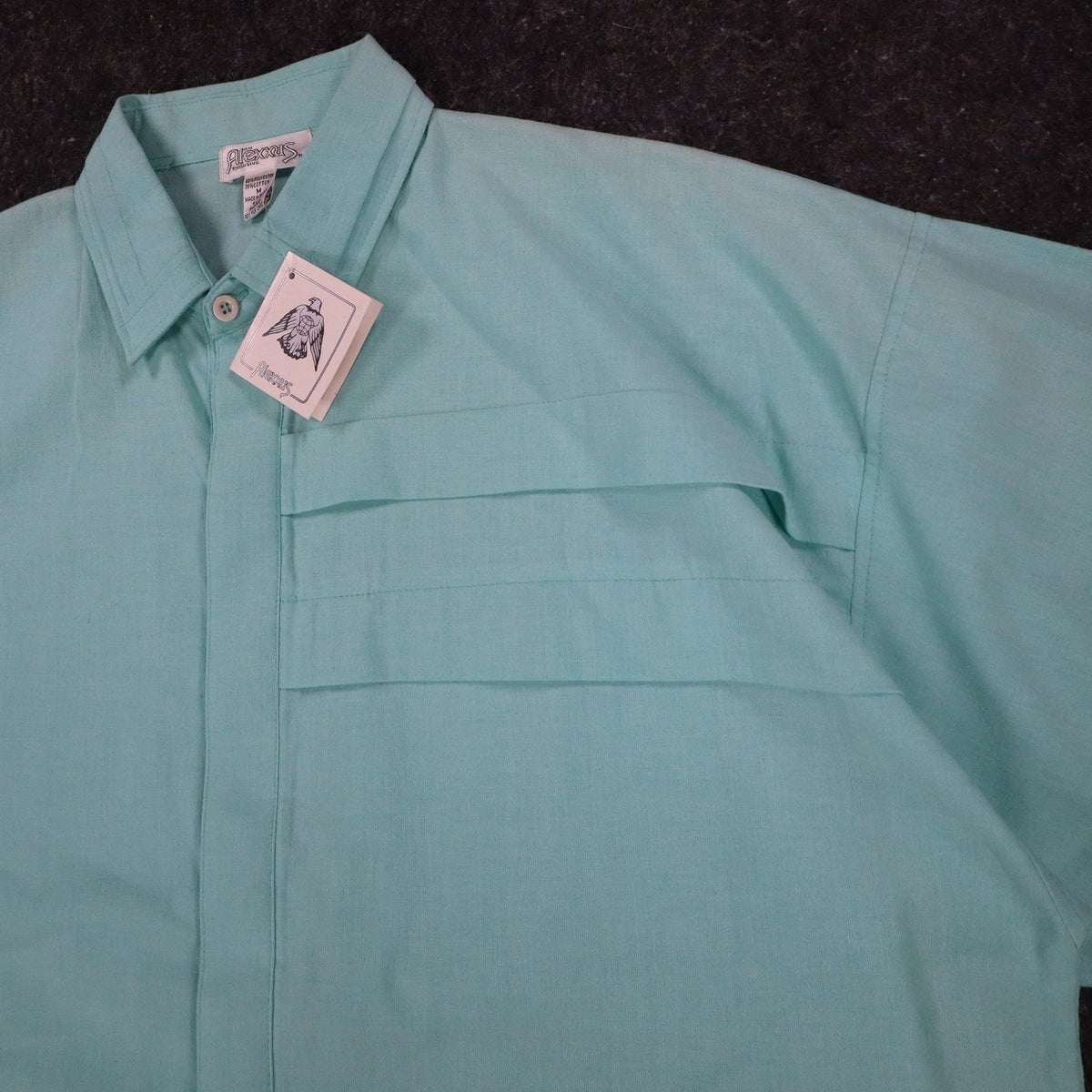 Angled close-up of the collar, front placket and chest pleats of an aqua blue Alexxus short-sleeve shirt