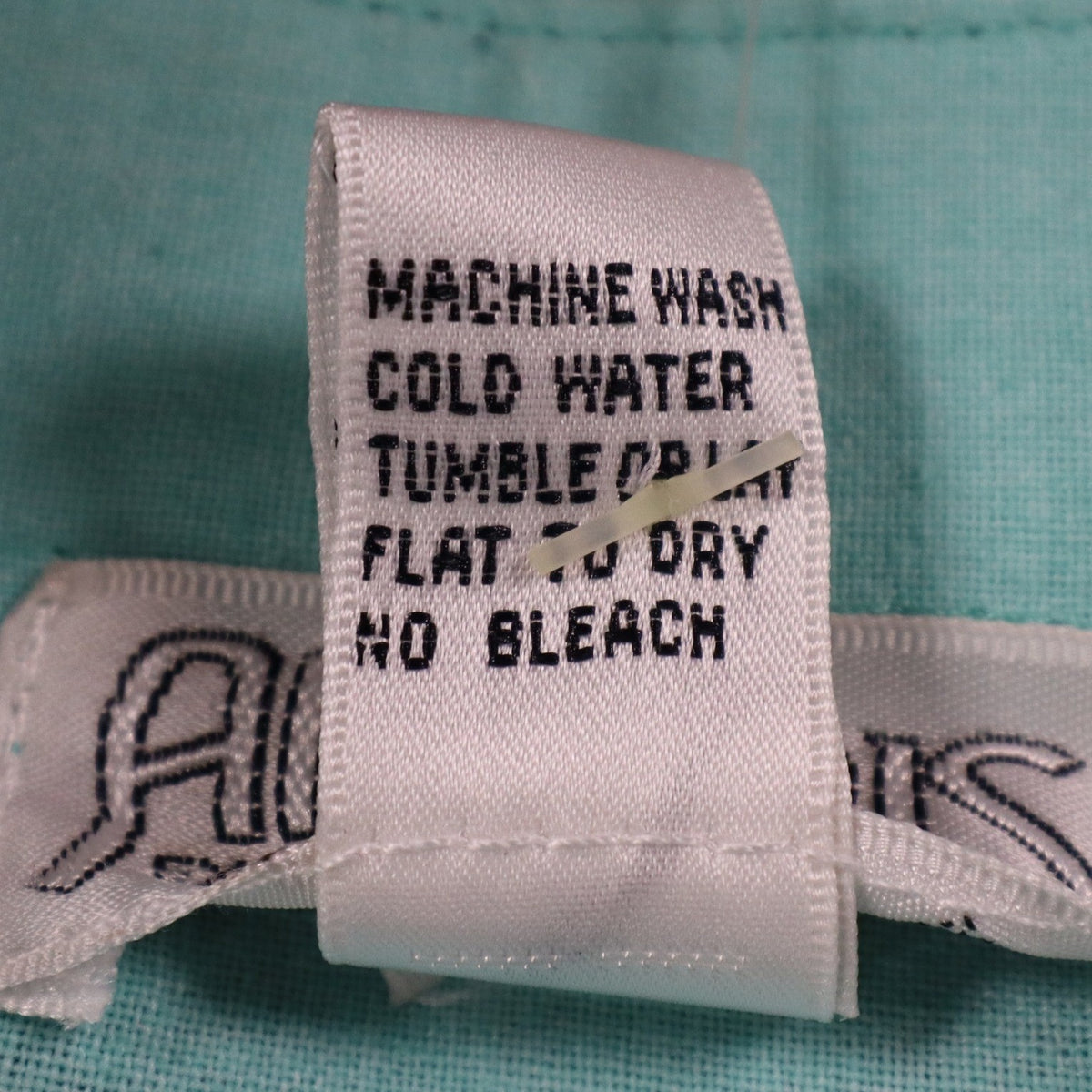Close-up of the care-instruction label inside aqua blue Alexxus short-sleeve shirt