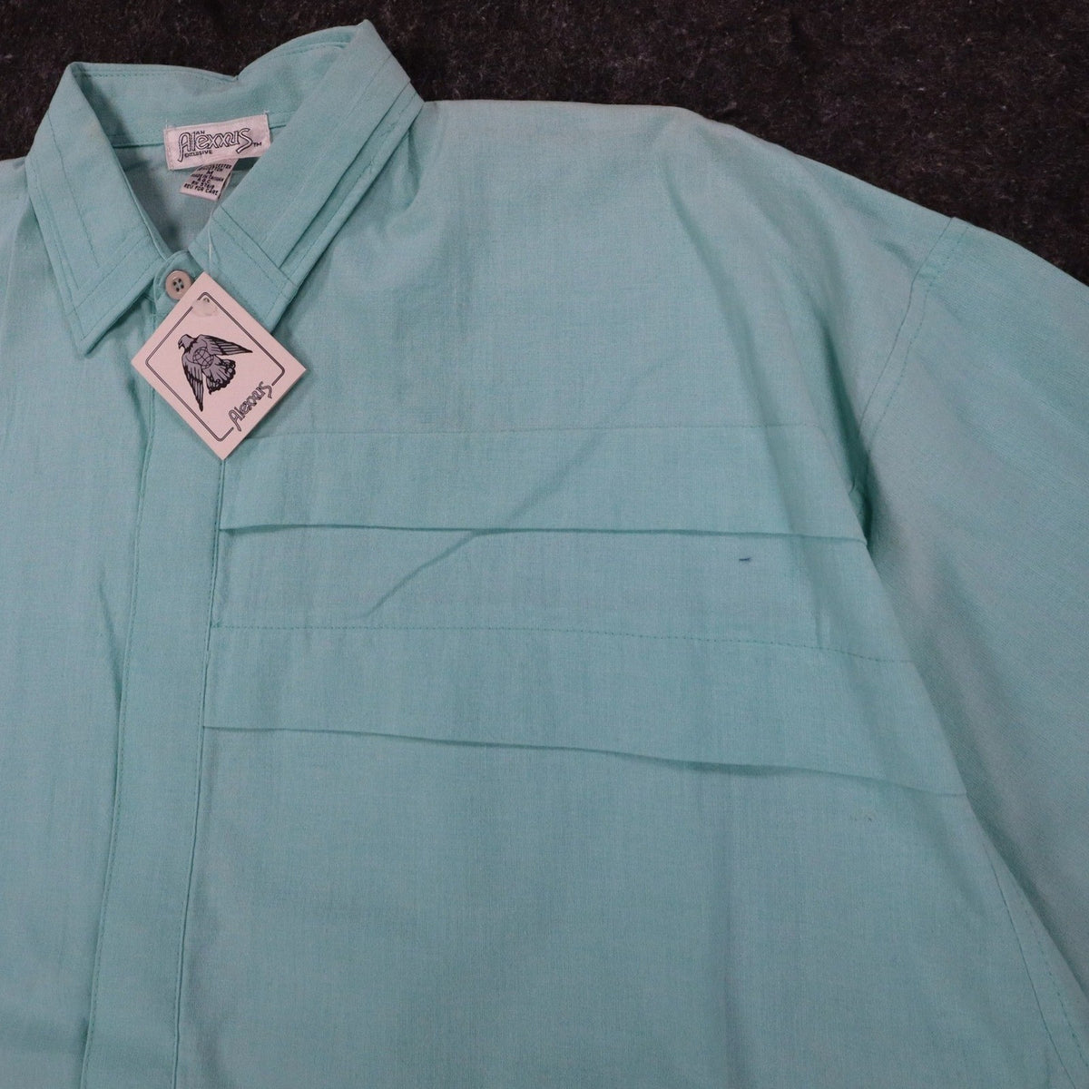 Angled close-up of the collar, front placket and chest pleats of an aqua blue Alexxus short-sleeve shirt